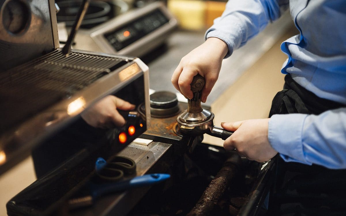 Barista tamping espresso behind the counter of a small coffee shop