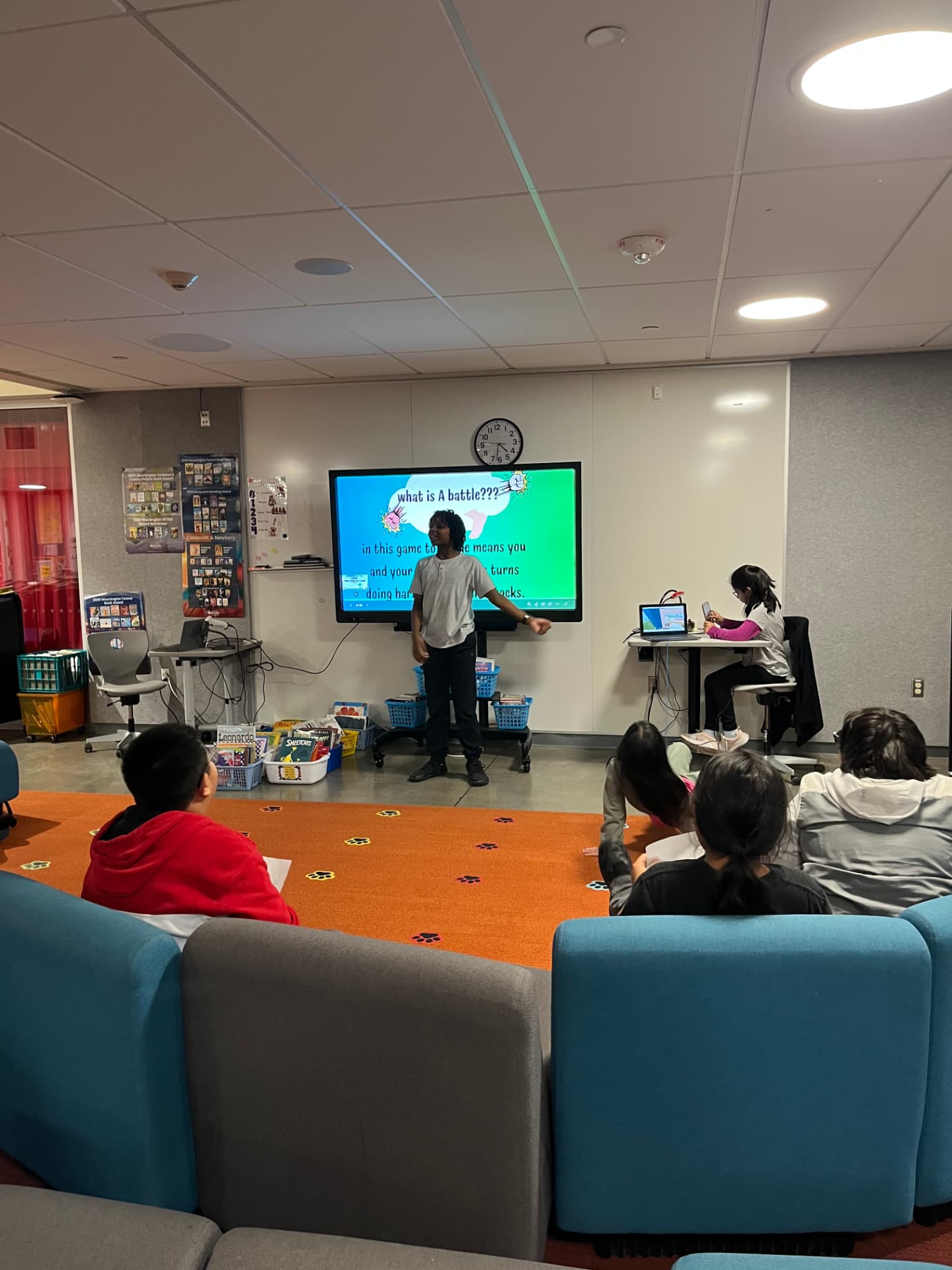 A student explains his game's battle mechanics on a classroom screen