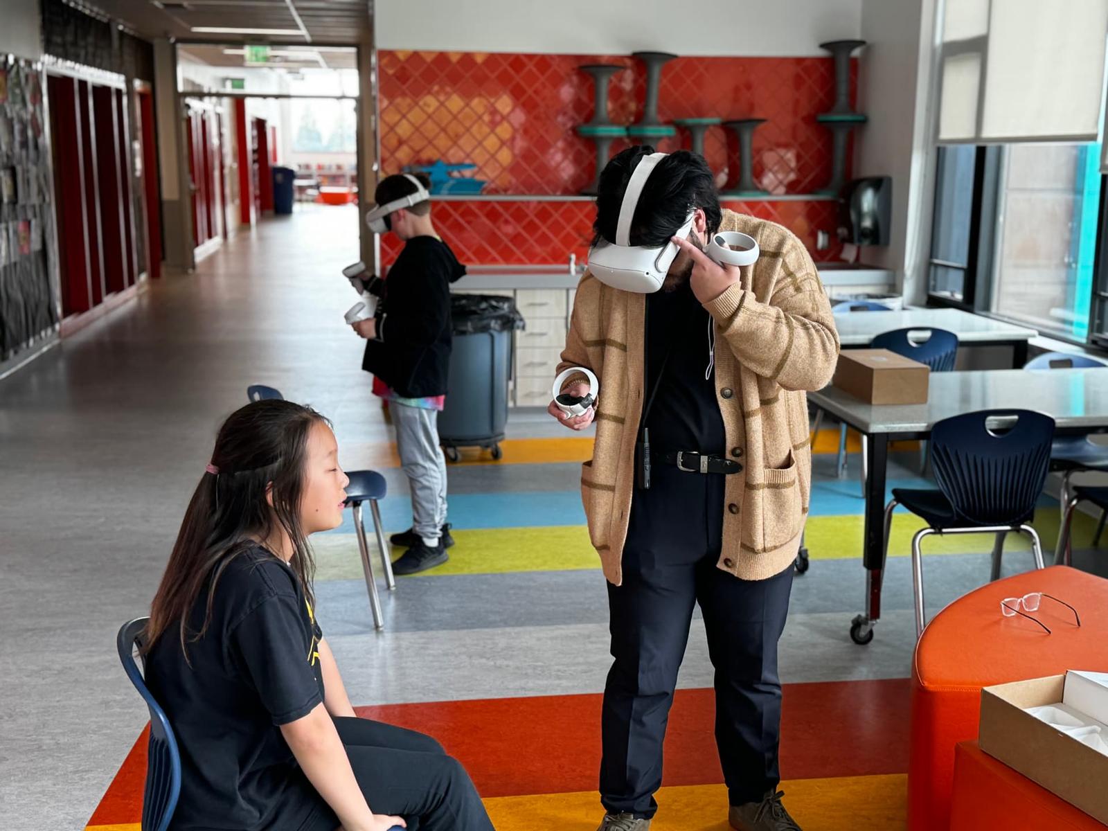 A BlackMuse instructor tries on a VR headset beside a seated student in a school commons